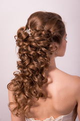 Wedding hairstyle on the head of a brown-haired woman in the back view on a white background close-up.
