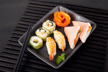 A set of sushi, sashimi from salmon and oriental snacks on a black plate.