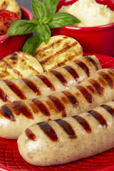 Food is still life. Three sausages of pork and zucchini on a red plate. Basil. Puree from potatoes and grilled vegetables. Black marble background.