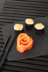 Three rolls in black seaweed and salmon sashimi on a black background.