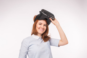 VR, technologies, people concept - surprised young woman looking at Virtual Reality Glasses and smiles over the white background.