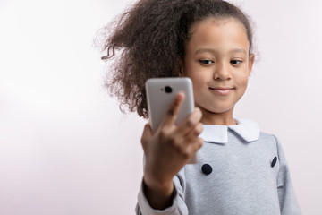 pretty girl with long wavy hair in ponytail is making a video call. positive kid is taking photos. isolated white nackground. close up portrait. device concept. blurred foreground.