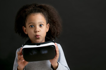 excited girl after watching the wearing virtual glasses. copy space. isolated black background. surprised kid having fun with VR glasses