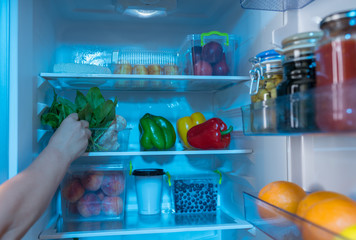 Hand reaching for bowl with spinach in open fridge © kolotype