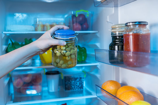 Hand reaching for jar with olives in fridge
