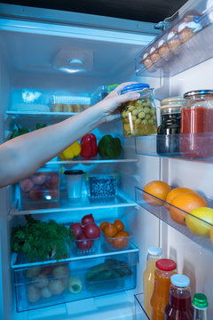 Hand reaching for jar with olives in fridge