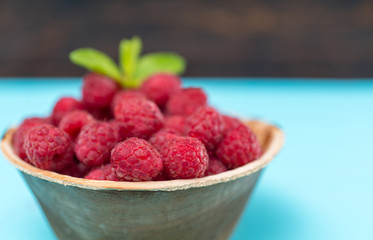 Bowl of juicy raspberries against blue table