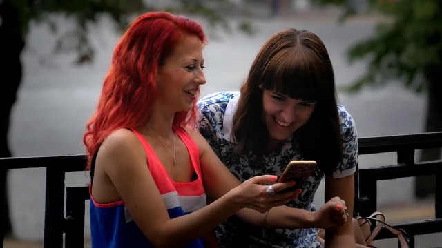 Smiling cheerful young women laughing about photos at mobile phone at the street 