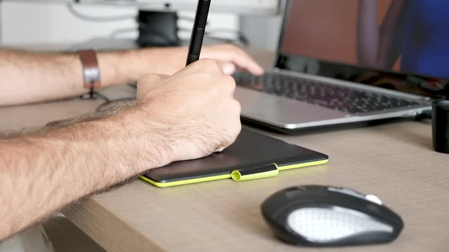 Professional graphical designer working on a digital tablet with a pen. Close up footage of artist at his desk