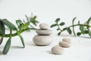 Fototapeta na wymiar Pyramids of white zen stones with green leaves on white background. Concept of harmony, balance and meditation, spa, massage, relax