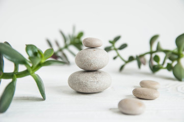 Fototapeta na wymiar Pyramids of white zen stones with green leaves on white background. Concept of harmony, balance and meditation, spa, massage, relax