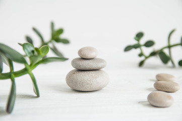 Obraz na płótnie Canvas Pyramids of white zen stones with green leaves on white background. Concept of harmony, balance and meditation, spa, massage, relax