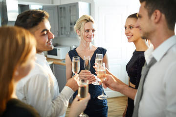 Group of young cheerful people with flutes of champagne making circle while talking and toasting at party