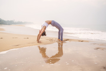 Caucasian woman practicing yoga at seashore of tropic ocean