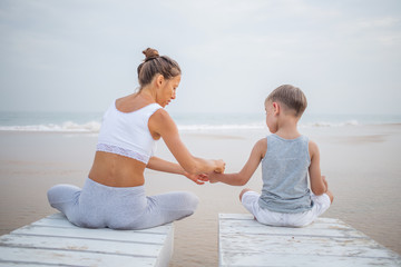 A mother and a son are doing yoga exercises at the seashore of tropic ocean