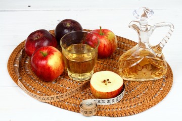Apple vinegar good for diet / Fersh apples, measuring tape, cut bottle and glass on white wooden table