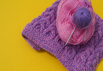 Coats of wool pink and purple lie next to an unconnected cap. Yellow background.