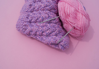 The process of knitting a lilac cap. Woolen threads on a pink background. Cozy yarn.