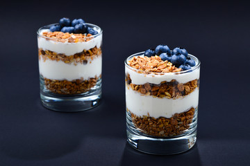 Homemade baked granola with yogurt and blueberries in a glass on a black background. Space for text or design.