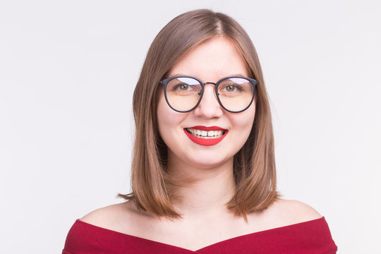Fashion and people concept - Close up portrait of young smiling woman in glasses with red lips on white background