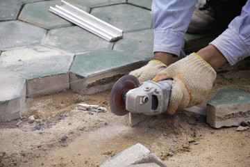 Workers cutting green concrete hexagonal blocks for patterned flooring.