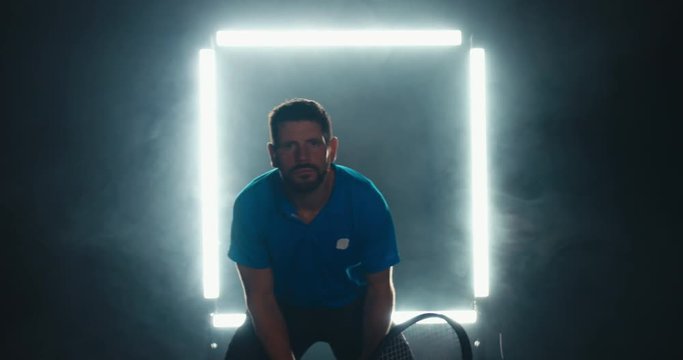 Caucasian male tennis player hitting a ball against dark background with square light. 4K UHD 60 FPS SLOW MOTION