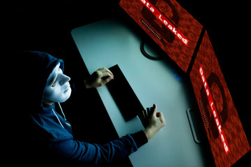 Masked hacker under hood using computer to hack into system and employ data leaking process - internet computer crime concept.