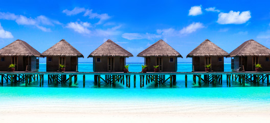Water villas on wooden pier in turquoise ocean on the white sand beach