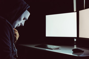 Masked hacker under hood using computer to hack into system and trying to commit computer crime - Hacker and computer threat crime concept.