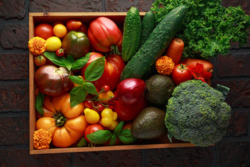 Organic Vegetable box with large, cherry tomatoes, basil, cucumbers, red onions, broccoli and avocado.