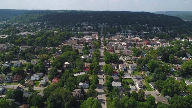 A slow reverse aerial establishing wide shot of the residential district of a small town in western Pennsylvania on a summer day. Pittsburgh suburbs.  	