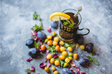 a glass of tea with lemon and scattered berries - blue and yellow plums