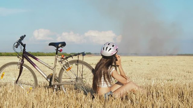 A cyclist in a burning field. A girl with a bicycle calls firefighters. Burning field.