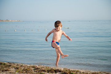healthy little boy kicking sea water with his leg on summer vacation beach
