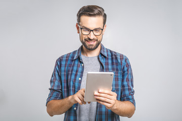 Happy young man in plaid shirt standing and using tablet over grey background