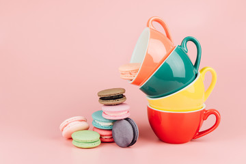 Colorful stack of cups for latte coffee with sweet french macaroons cake in a vintage pastel colored tone on pink background with copy space.