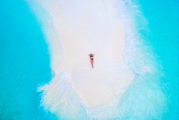 Beautiful woman tans on sandbank surrounded by turquoise ocean from above - obrazy, fototapety, plakaty