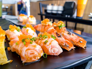 Sushi Shrimp burn the fire (Aburi River Prawn) and Aburi Salmon sushi with sauce and Tamagoyaki Sandwich put on a black plate in Japanese restaurant.