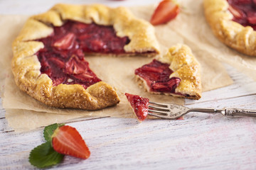 Baked galette or open pie with strawberry on white wooden background
