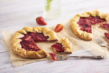 Baked galette or open pie with strawberry on white wooden background