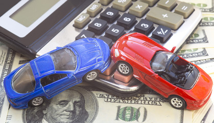 concept of car accident loss and damage. Calculator on the heap of us hundred dollars. two model cars above calculator.