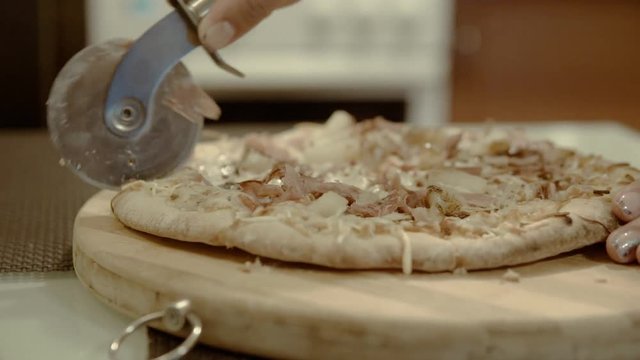 Female cuts the pizza on a wooden cutting board in the kitchen close-up 4k.