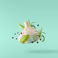 Garlic falling in air with pepper and herbs like rosemary on turquoise background.
