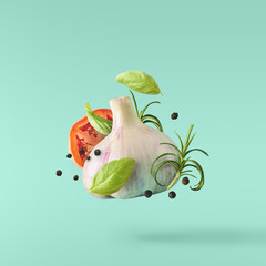 Garlic falling in air with pepper and herbs like rosemary on turquoise background.
