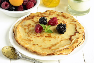 Сrepes, fresh berries and honey on wooden background