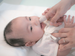 Mother use finger to clean asian baby tongue with clean gauze.