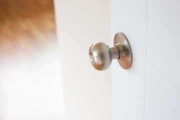 Stainless door knob on the luxury white wooden door close up with blurred room and environment in background.