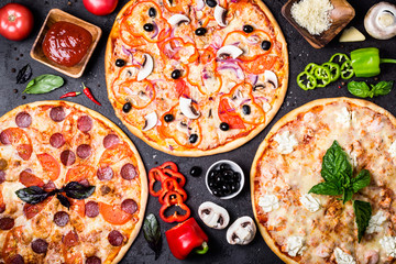 selection of different pizzas on a black background and ingredients. Peperoni, Vegetarian and...