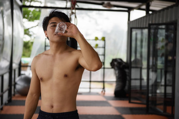 Fototapeta na wymiar Thirsty Asian fitness man drinki water in gym