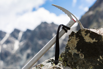 an ice axe on a stone against high rocky mountain range and blue sky with some white clouds